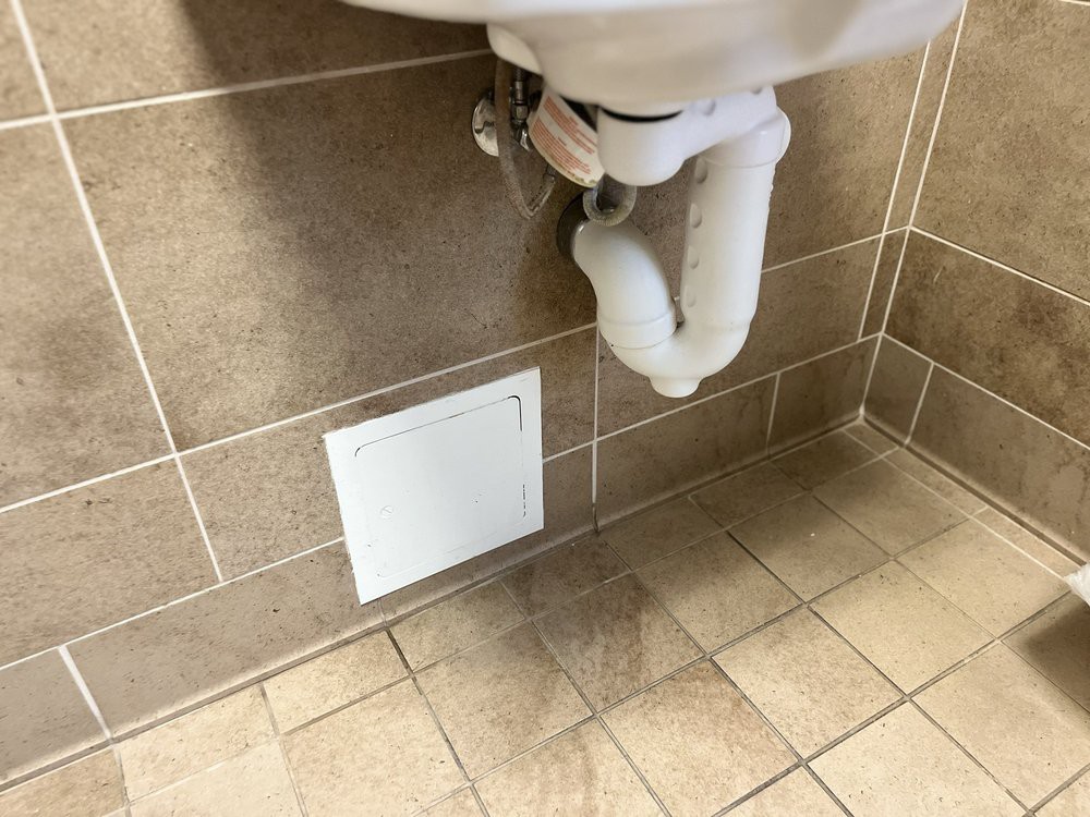 A bathroom sink with visible plumbing and a wall vent beneath it.