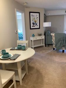 A cozy living and dining space featuring a small table set with teal dishes, a comfortable chair, and tasteful decor.