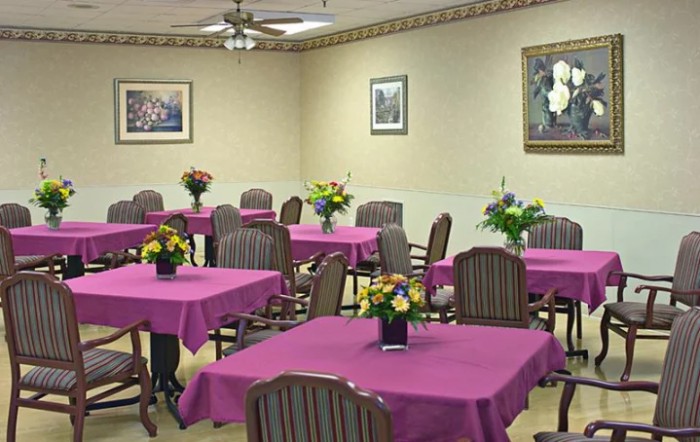 A dining room with multiple tables decorated with purple tablecloths and floral centerpieces.
