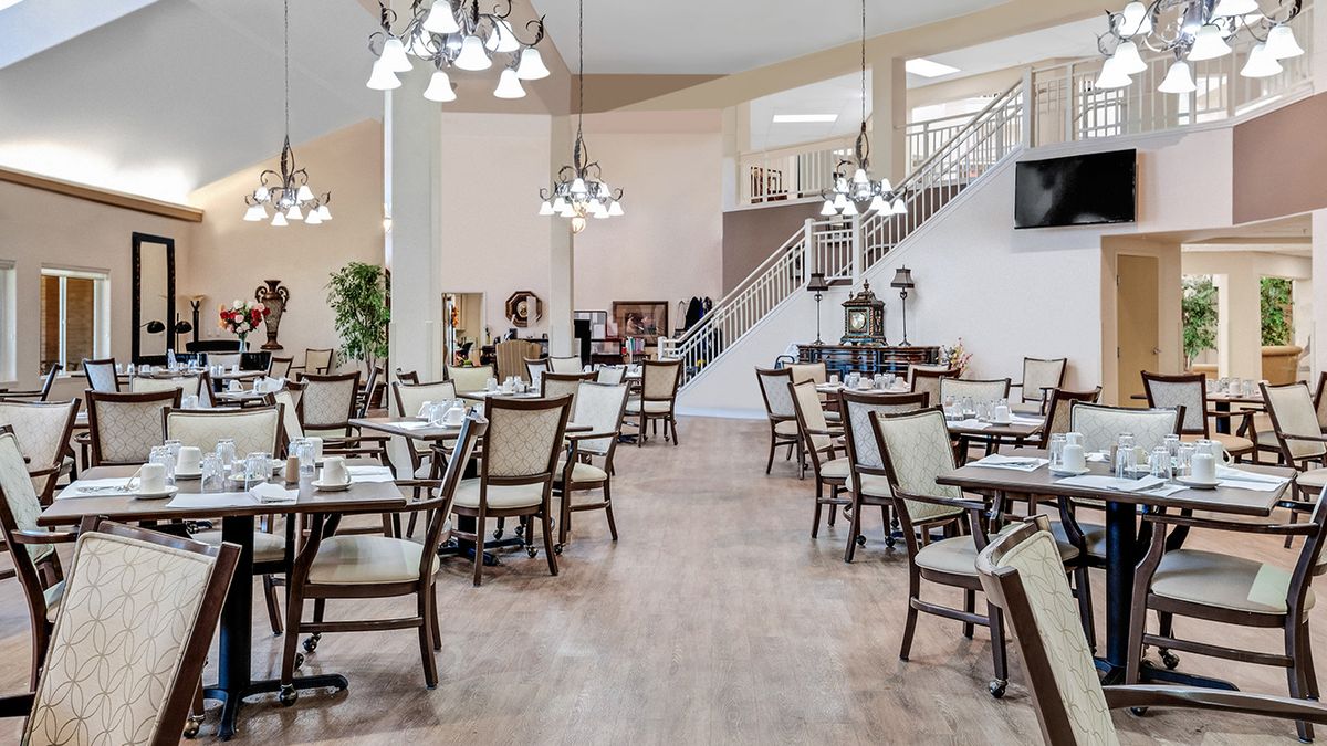 A spacious dining area featuring multiple tables and chairs, elegant chandeliers, and a wooden floor.