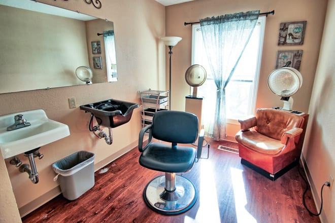 A cozy hair salon with a styling station, featuring a salon chair, mirror, sink, and hair dryer.