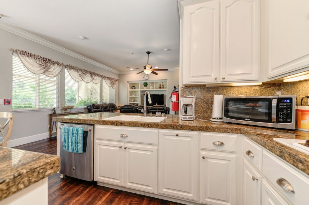 A well-lit kitchen with white cabinets, a granite countertop, and various appliances.