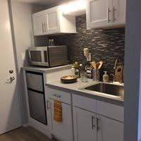 A compact modern kitchen with a sleek design, featuring a microwave, small oven, and stylish backsplash.