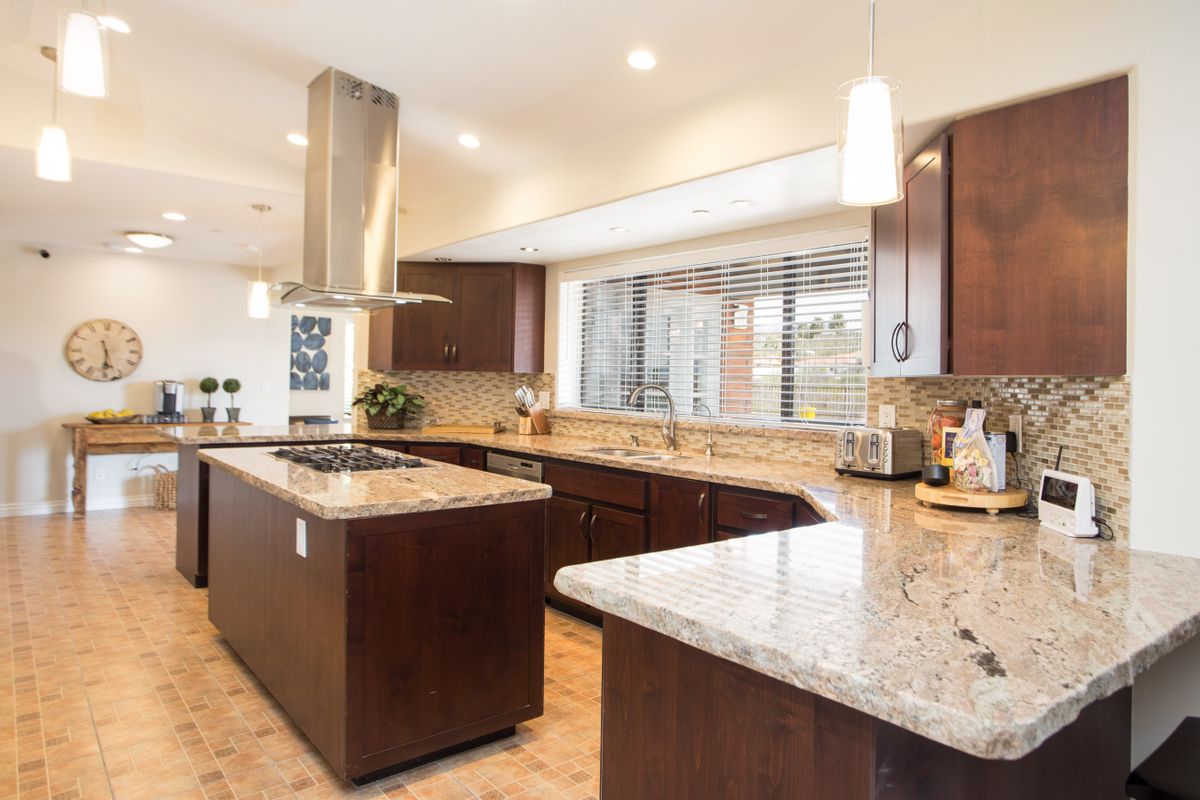 A spacious modern kitchen with a central island, wood cabinets, and granite countertops.