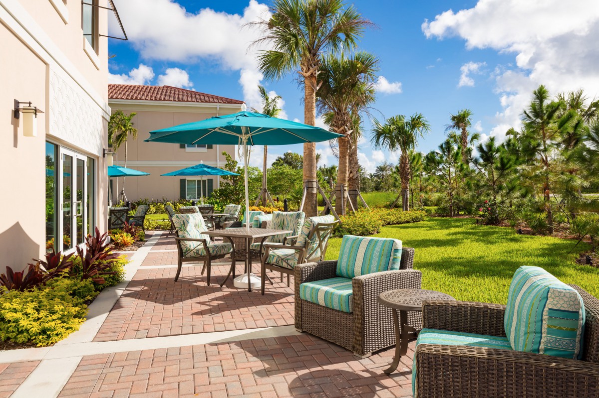 A beautifully landscaped outdoor patio with comfortable seating and umbrellas, surrounded by palm trees on a sunny day.