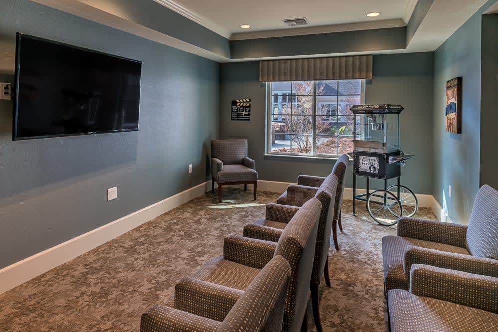A cozy theater room with several chairs facing a television and a popcorn machine by the window.
