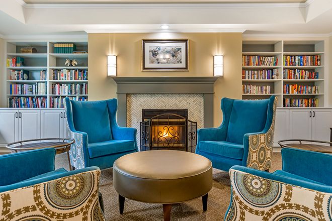 A cozy living room with a fireplace, blue armchairs, and surrounding bookshelves.
