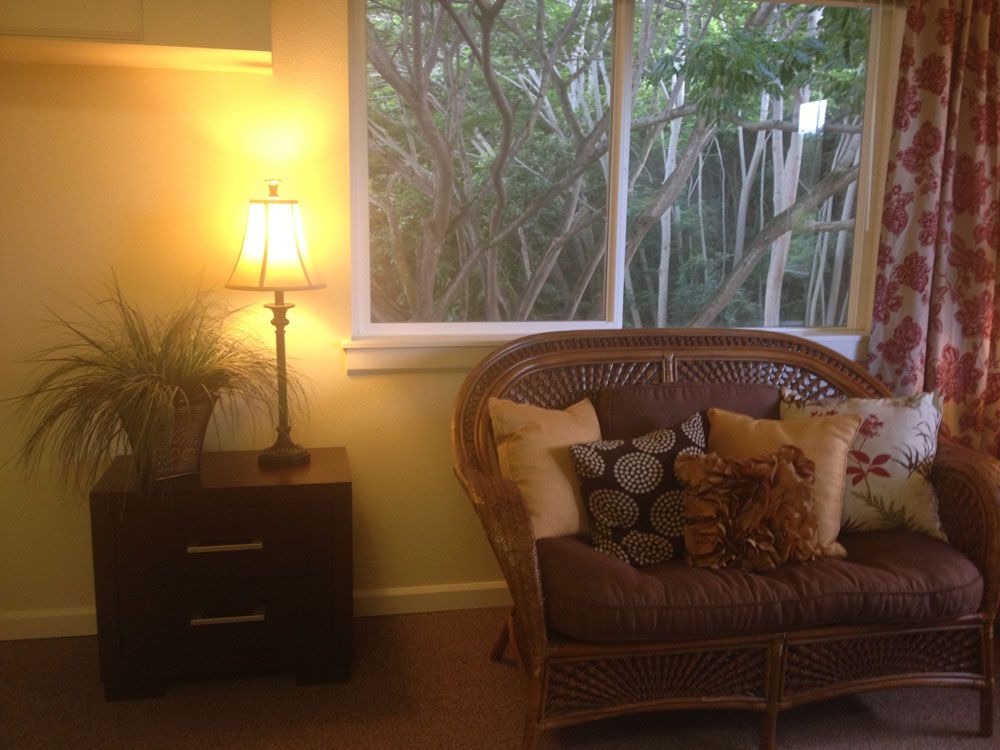 A cozy living room with a wicker sofa and cushions next to a warmly lit lamp.