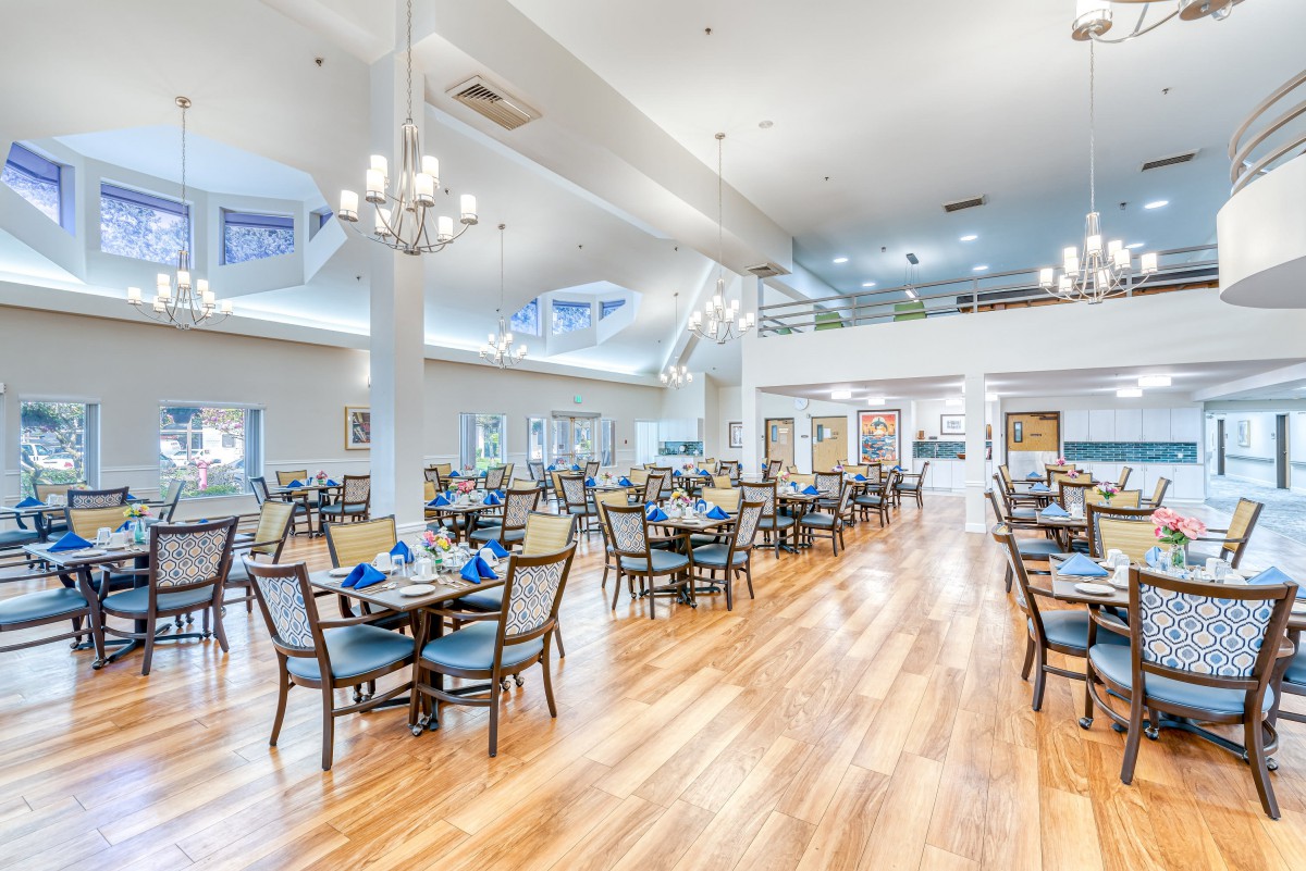 A spacious and elegantly designed dining room with multiple tables and chairs, featuring chandeliers and a polished hardwood floor.