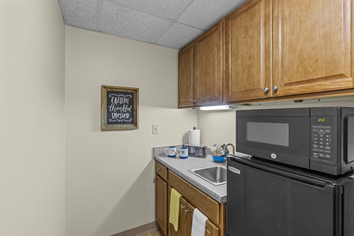 Small kitchenette with microwave, sink, and wooden cabinets.