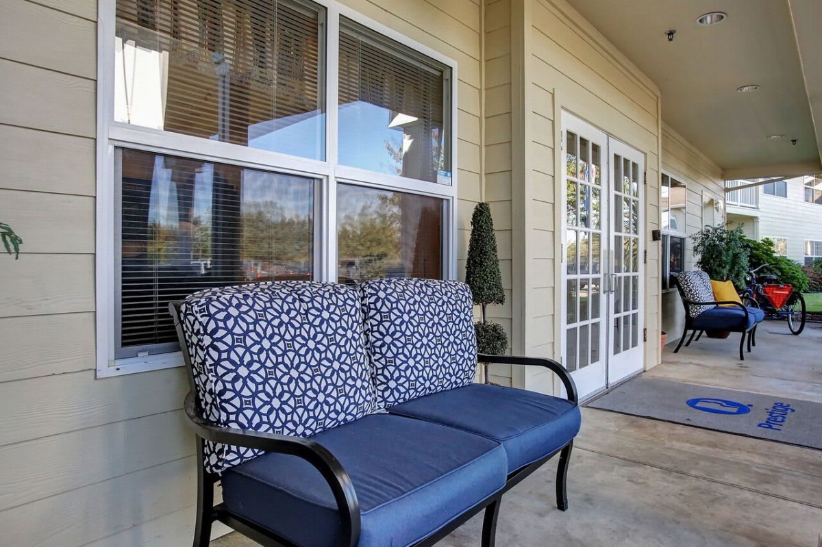 A cozy outdoor patio area featuring a cushioned bench near large windows and French doors.