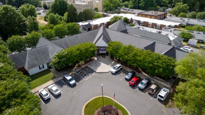 Aerial view of a building with a surrounding parking lot and landscaped entrance.