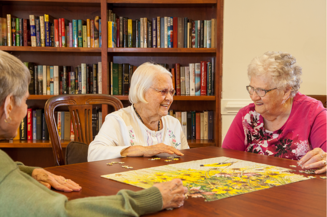 A group of seniors enjoying a puzzle together in a library setting.