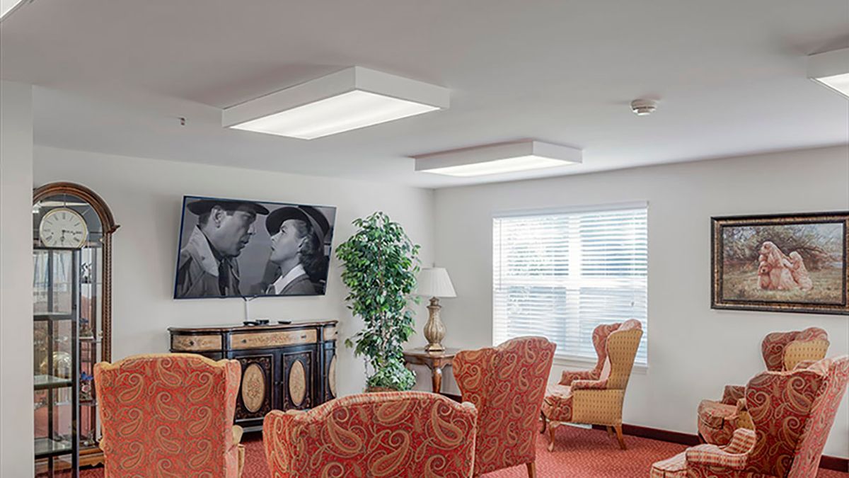 A cozy living room with red upholstered chairs, a vintage-style cabinet, and a television displaying a black and white movie scene.