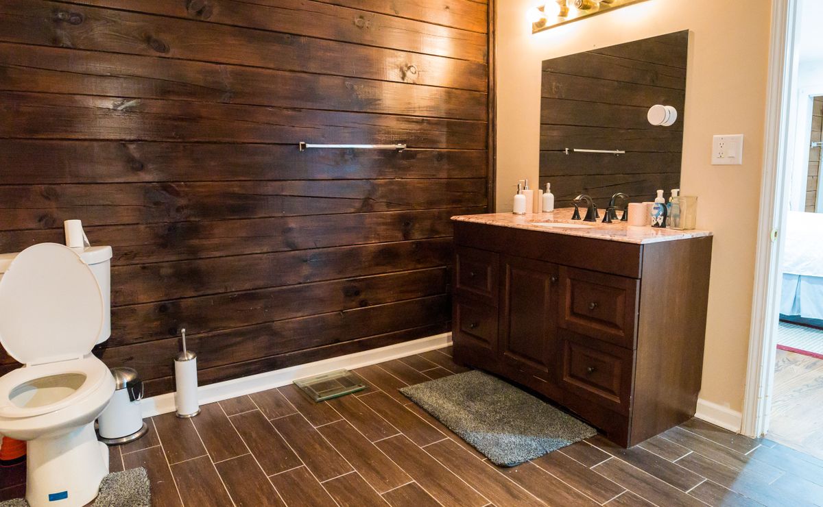 A modern bathroom with wooden walls, featuring a vanity with a mirror and sink.