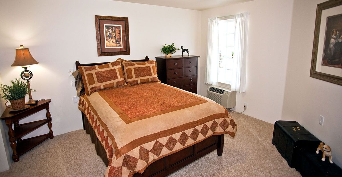 A cozy bedroom featuring a neatly made bed with a patterned quilt, a dresser, and a framed artwork above the headboard.