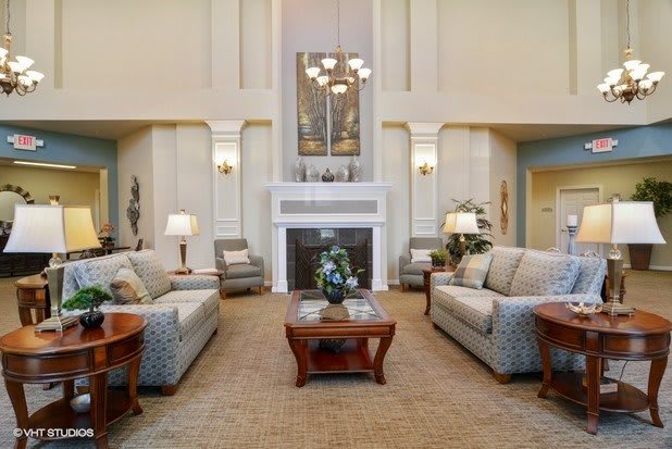 A spacious living room with elegant furnishings, featuring sofas, a central coffee table, and a fireplace under a chandelier.