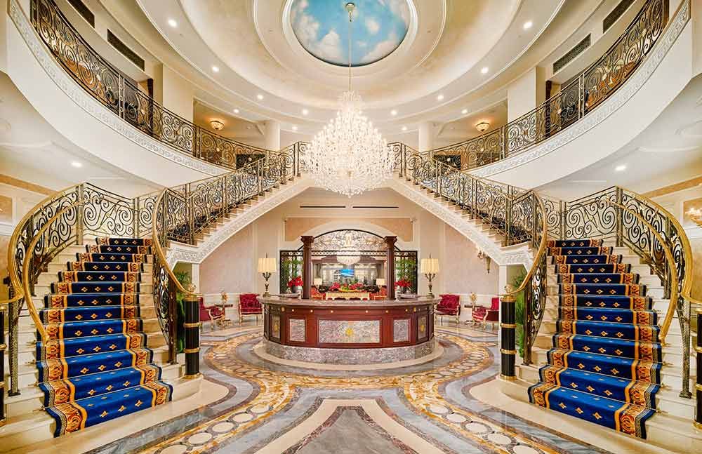 A luxurious hotel lobby featuring a grand staircase and an ornate chandelier.