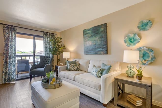 A cozy and stylish living room with a sofa, armchair, decorative pillows, artwork, and warm lighting.