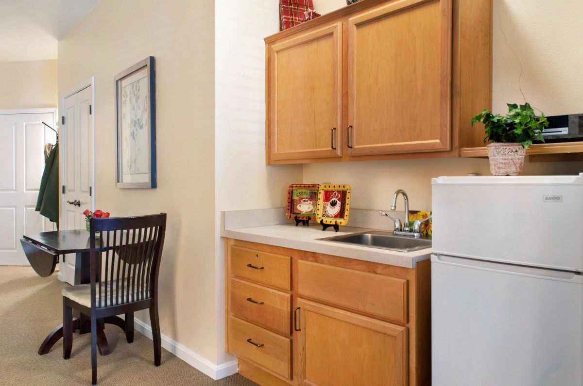 A compact kitchenette featuring wooden cabinets, a countertop with a sink, and a small refrigerator.