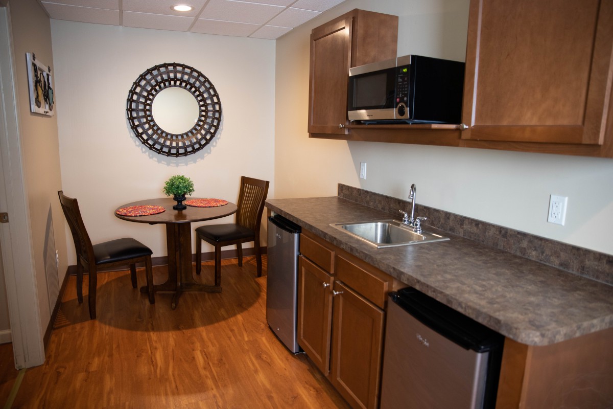 A compact, modern kitchen with wooden cabinets and a small dining area featuring a round table and chairs.