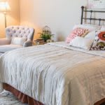 A cozy bedroom with a neatly made bed, an armchair, and soft lighting.