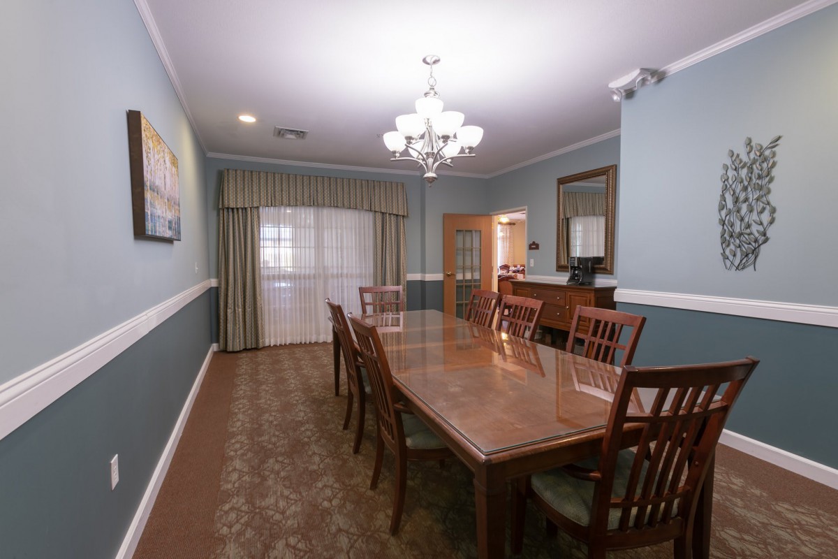A well-furnished dining room with a long wooden table and chairs, adorned by a chandelier.