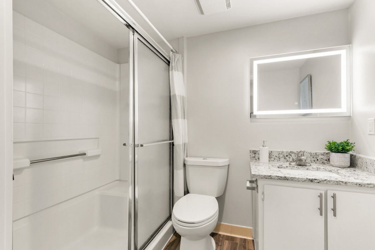 A modern bathroom featuring a shower, toilet, and vanity with a backlit mirror.