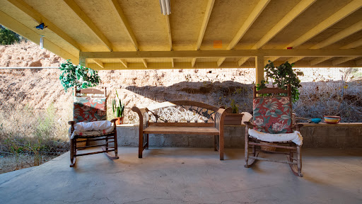 A cozy outdoor seating area featuring a wooden bench and rocking chairs, adorned with floral cushions, set against a decorative wall.