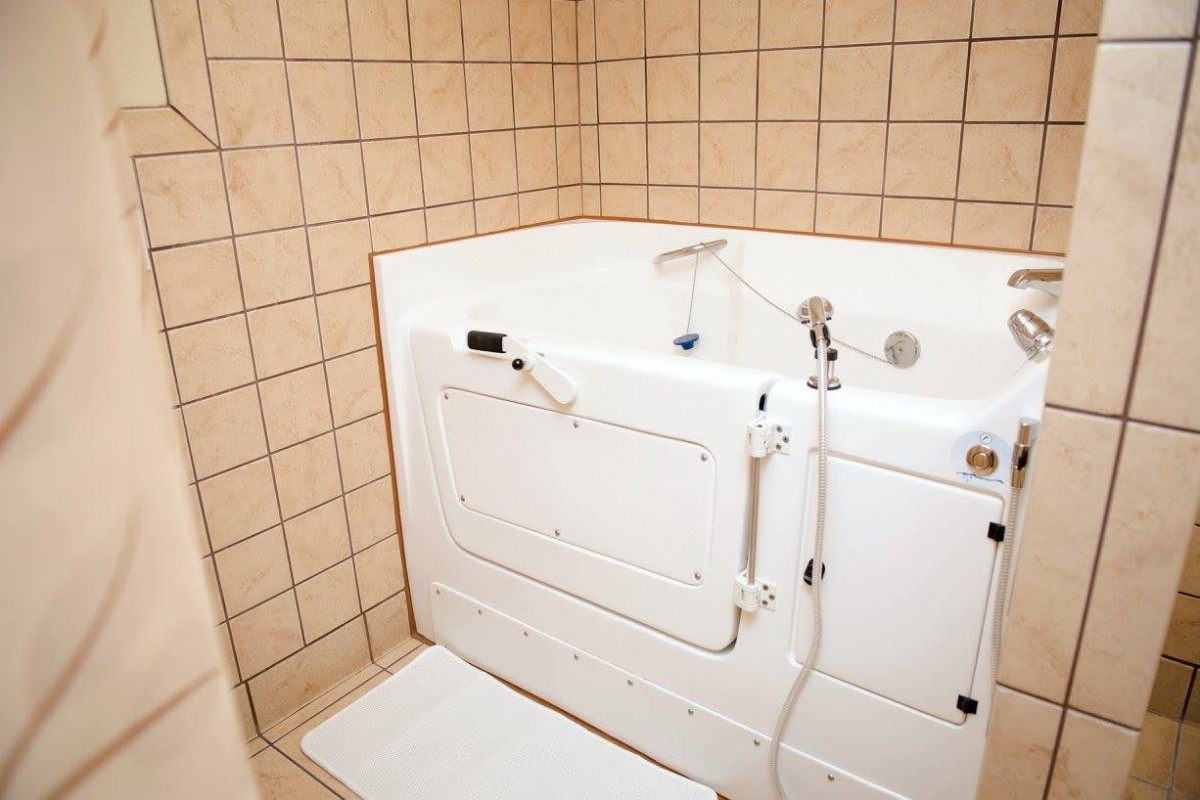 An accessible walk-in bathtub with tiled walls in a bathroom.