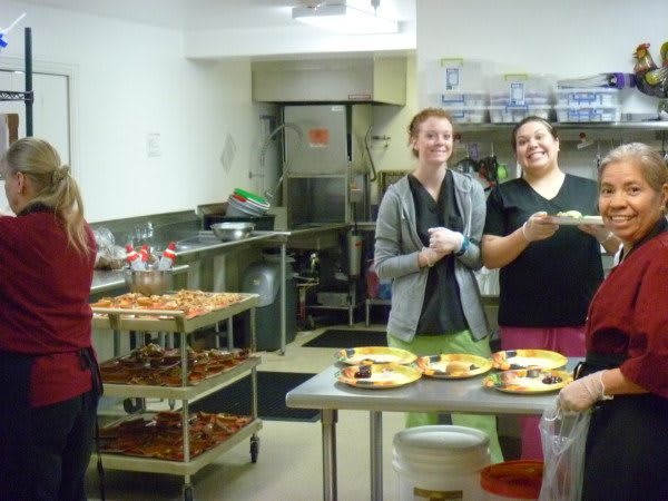 A group of people laughing and preparing food in a kitchen.