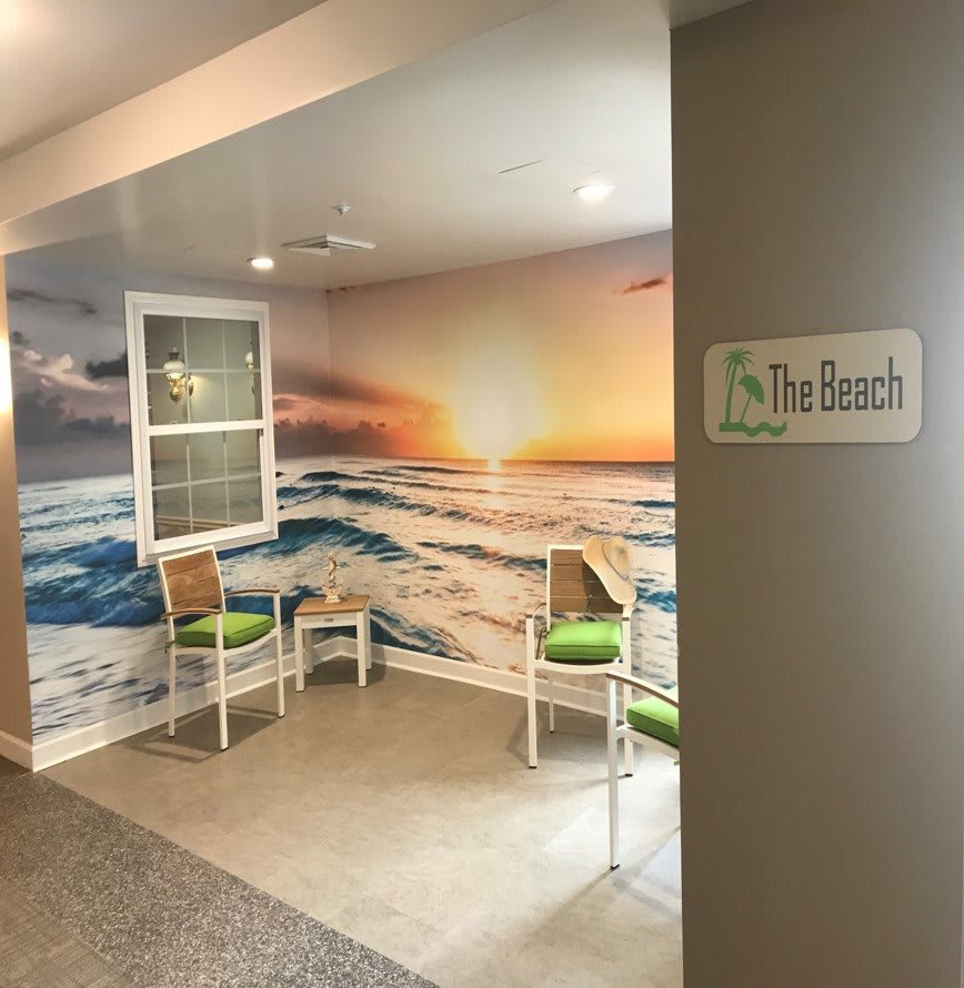 A cozy indoor seating area with chairs and a mural of a sunset over the ocean.