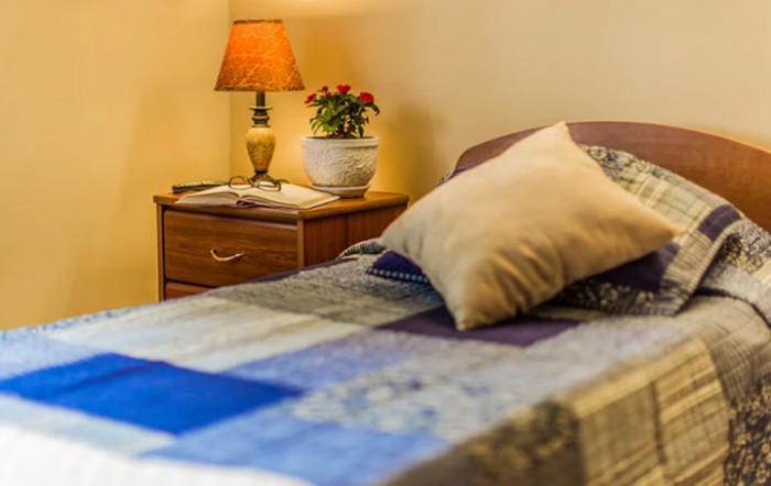 A cozy bedroom with a quilted bed, nightstand, and lamp.