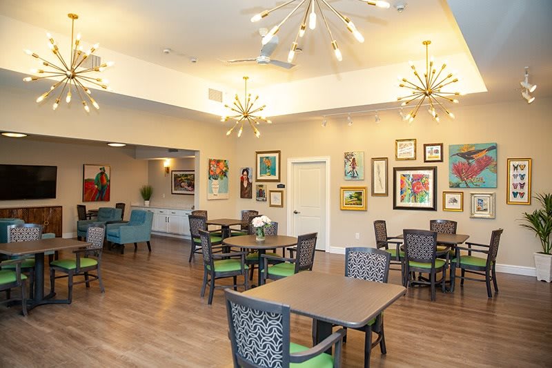 A modern dining room with eclectic artwork, stylish chandeliers, and neatly arranged tables and chairs.