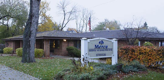 A healthcare facility named Mercy with a visible sign and surrounding autumn foliage.