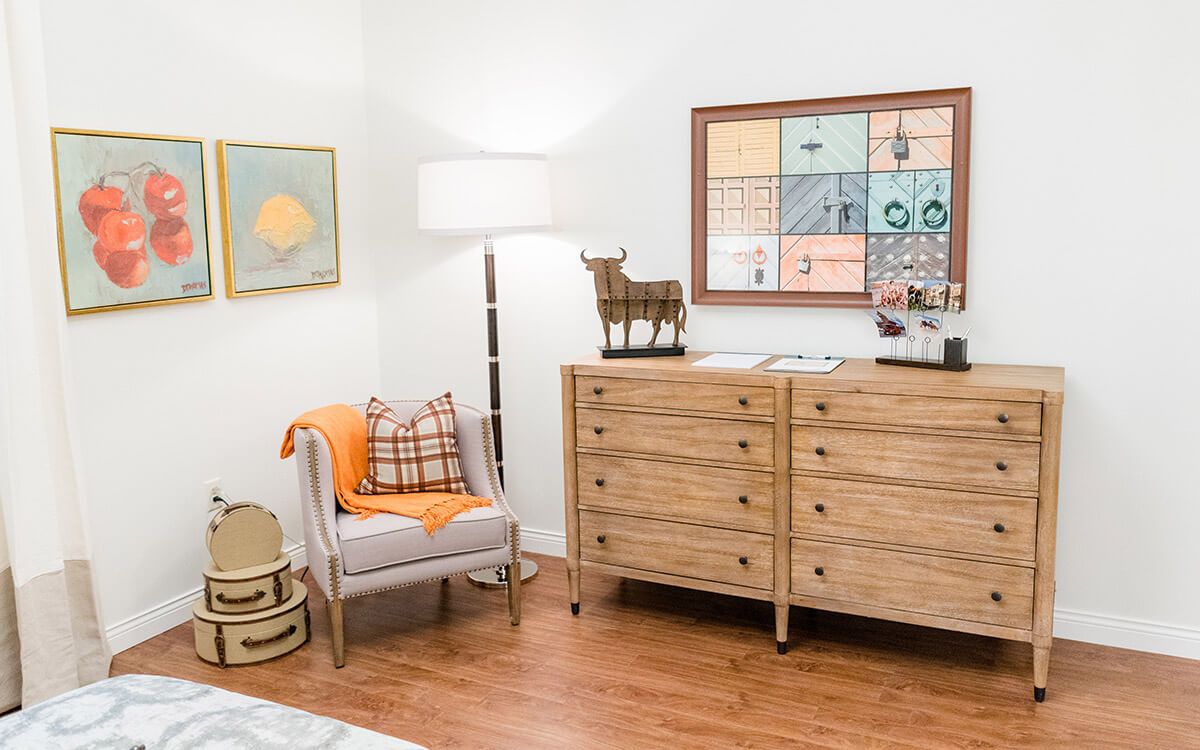 A modern bedroom with a wooden dresser, cozy chair, and decorative artwork.