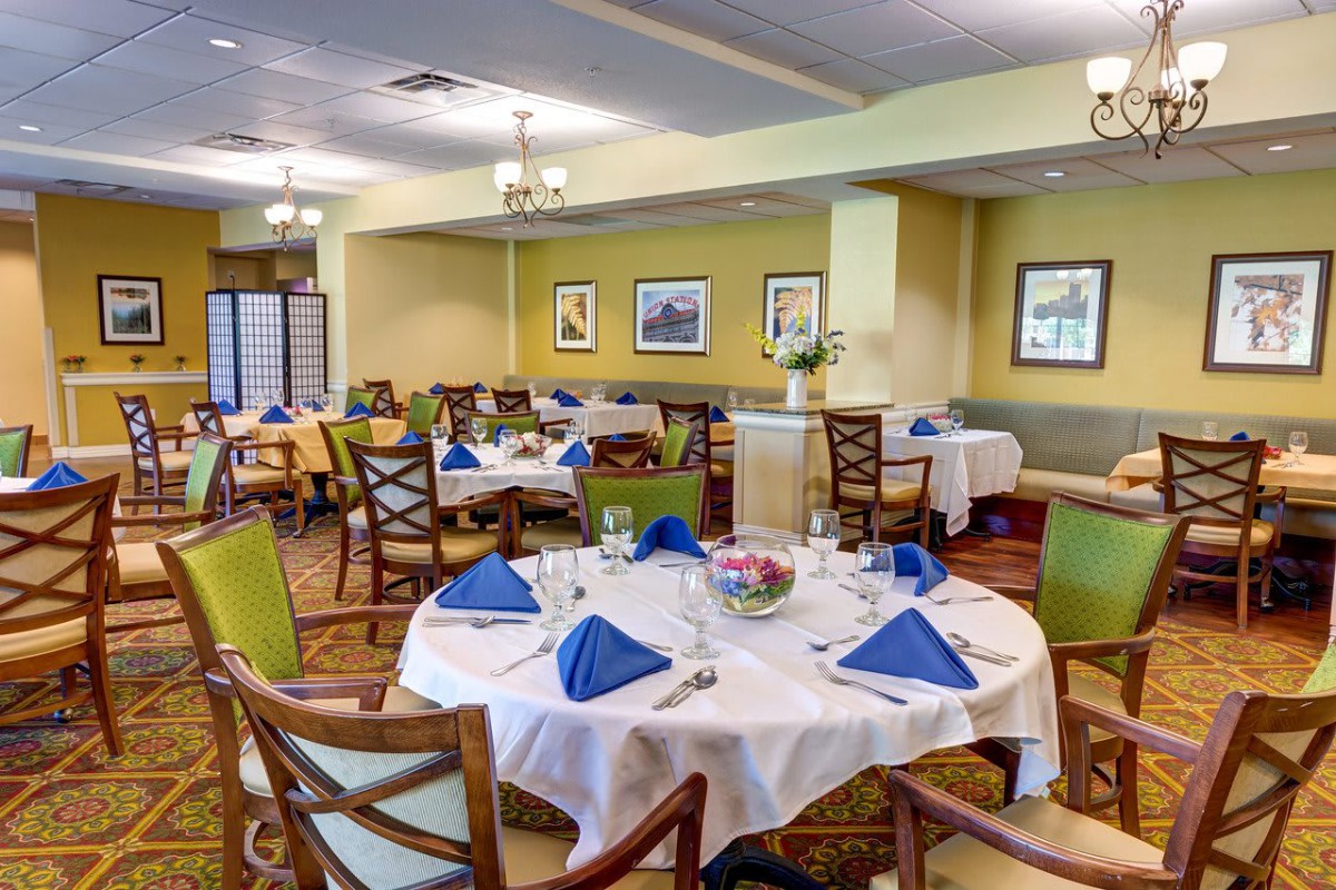 A cozy restaurant dining area with multiple tables set for guests, featuring blue napkins and elegant decor.