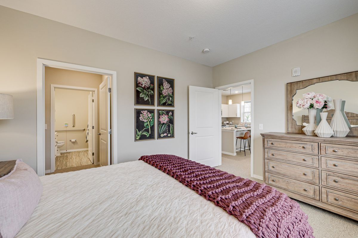 A cozy bedroom with a neatly made bed, artwork on the walls, and a dresser.