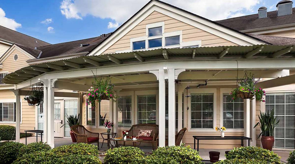 A cozy house with a covered porch and outdoor seating, surrounded by a lush garden.