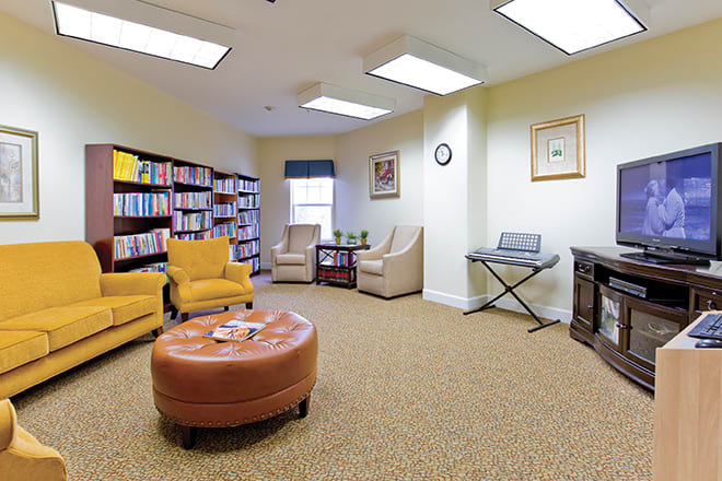 A cozy reading room with bookshelves, comfortable chairs, a round ottoman, and a piano keyboard.