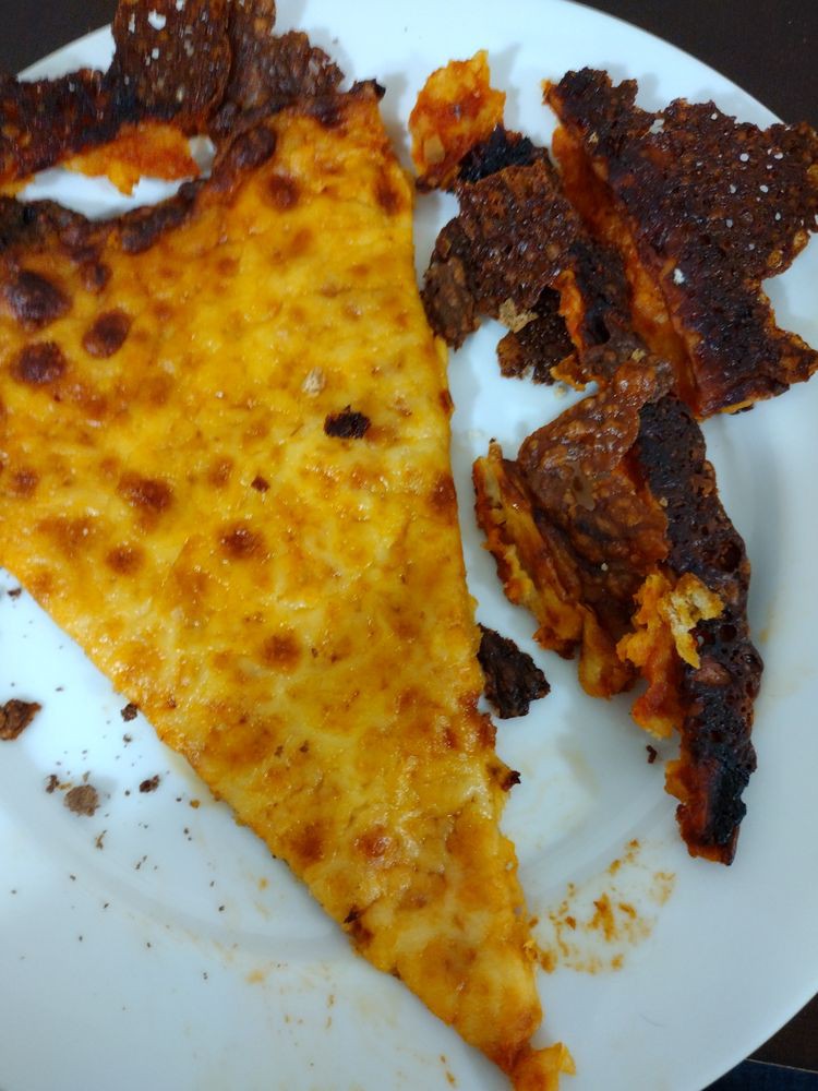 A slice of pizza with a burnt crust on a plate.