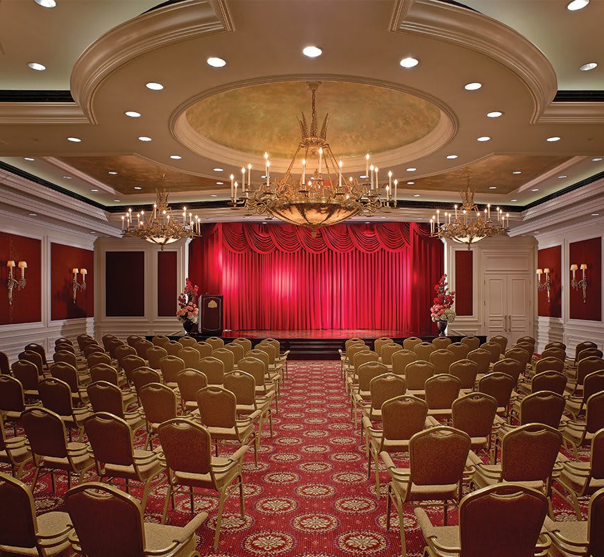 Elegant theater setup with rows of seating and a stage with red curtains.