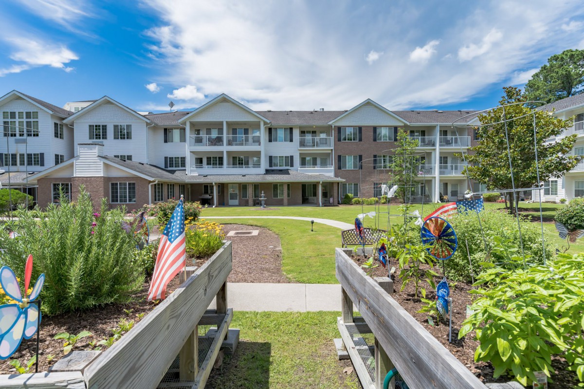 A scenic view of a residential building with gardens and flags under a partly cloudy sky.