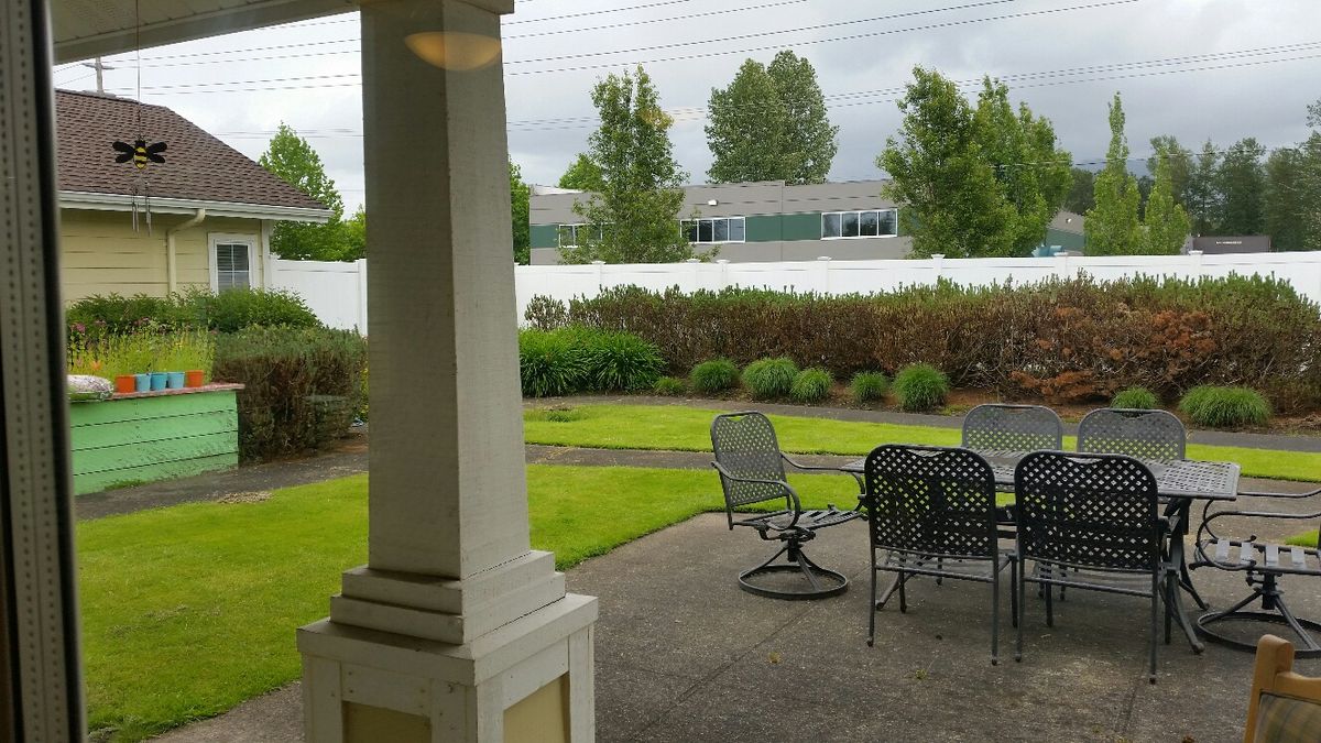 A backyard view featuring a patio with outdoor furniture, a manicured lawn, and surrounding trees.