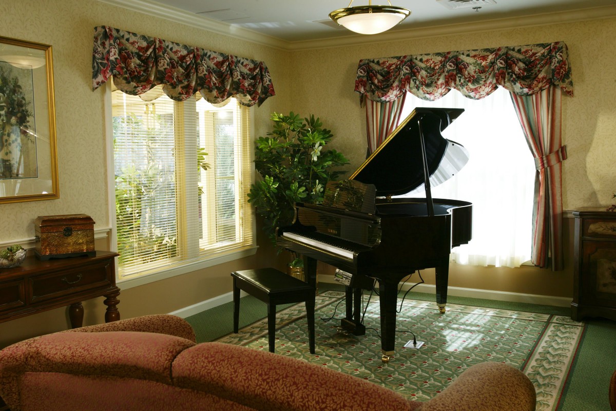 A grand piano in a cozy living room with large windows and elegant decor.