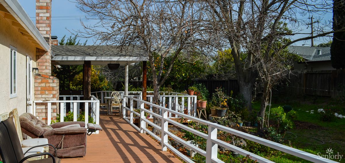 A peaceful garden pathway with a white fenced walkway leading to a pergola surrounded by lush greenery.