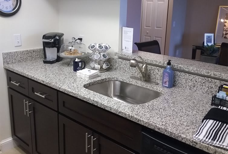 A kitchen with a granite countertop featuring a sink, coffee maker, and soap dispenser.