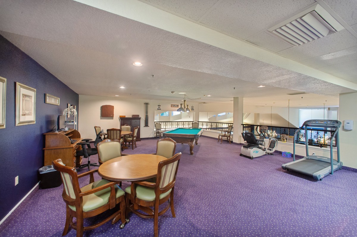 A spacious game and leisure room featuring a billiard table, exercise equipment, and seating area.