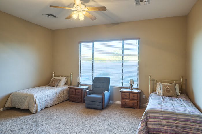 A cozy bedroom with two single beds, an armchair, and a large window.