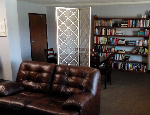 A cozy living room featuring a brown sofa, bookshelves filled with books, and a decorative partition.